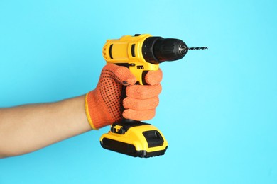 Photo of Man with cordless electric drill on light blue background, closeup. Space for text