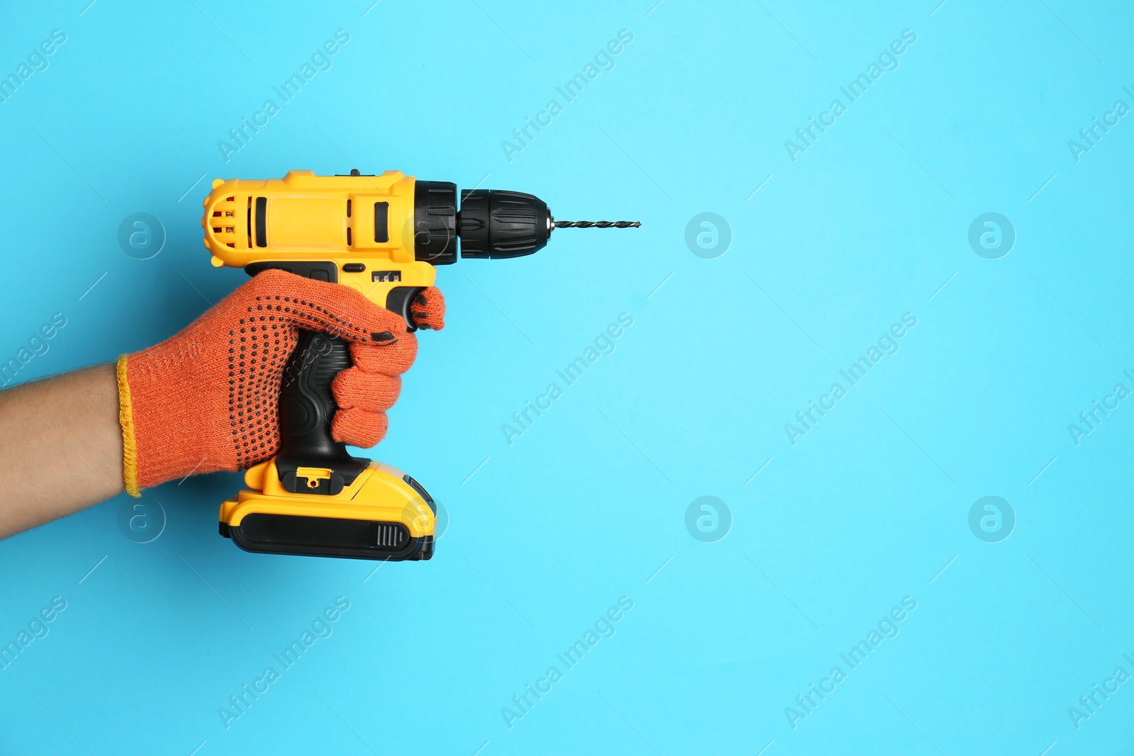 Photo of Man with cordless electric drill on light blue background, closeup. Space for text