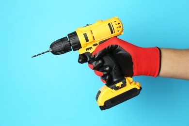 Photo of Man with cordless electric drill on light blue background, closeup. Space for text