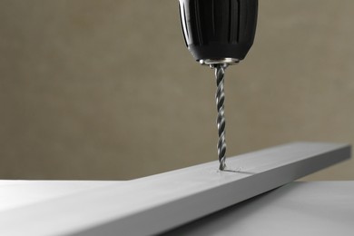 Photo of Drilling hole in light plank on table against gray background, closeup. Space for text