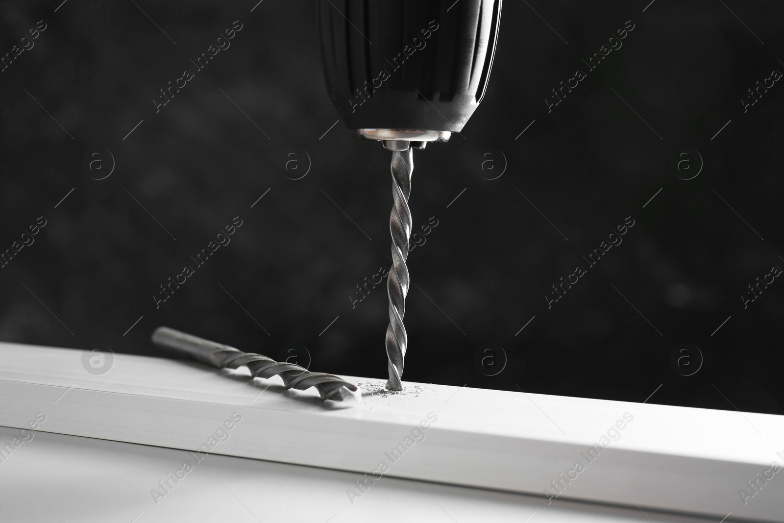 Photo of Drilling hole in plank on white table against black background, closeup