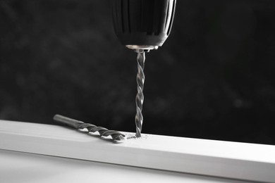 Photo of Drilling hole in plank on white table against black background, closeup