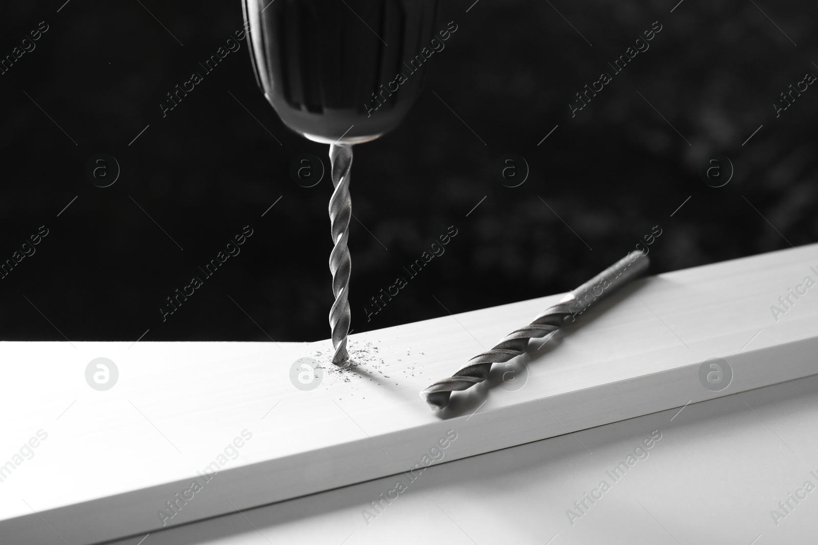 Photo of Drilling hole in plank on white table against black background, closeup