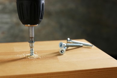 Screwing screw into wooden plank against gray background, closeup