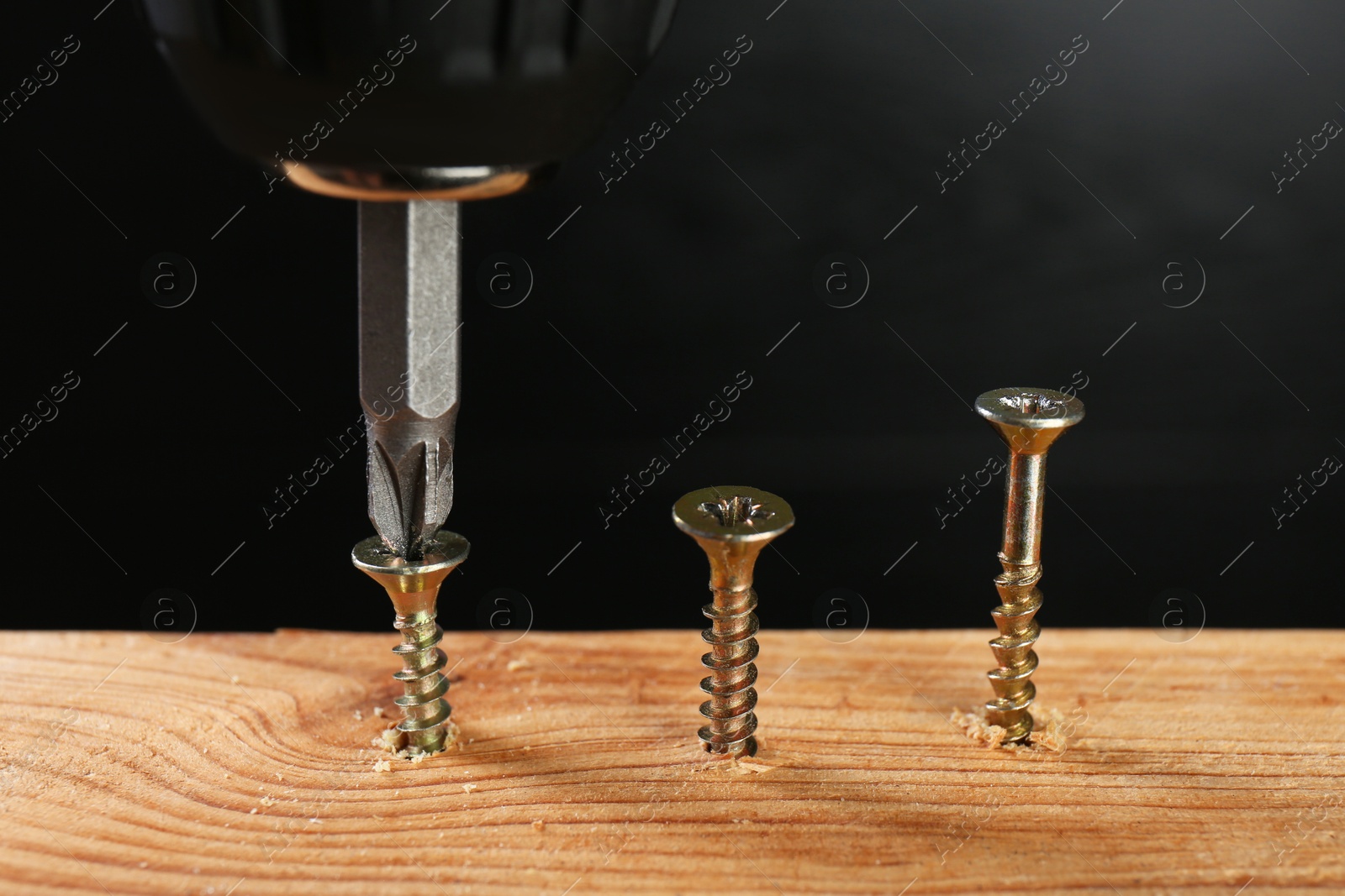 Photo of Screwing screw into wooden plank against dark background, closeup