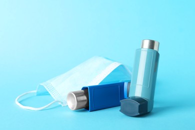 Photo of Asthma inhalers and medical mask on light blue background, closeup