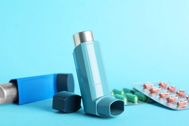 Photo of Inhalers and pills on light blue background, closeup. Asthma treatment