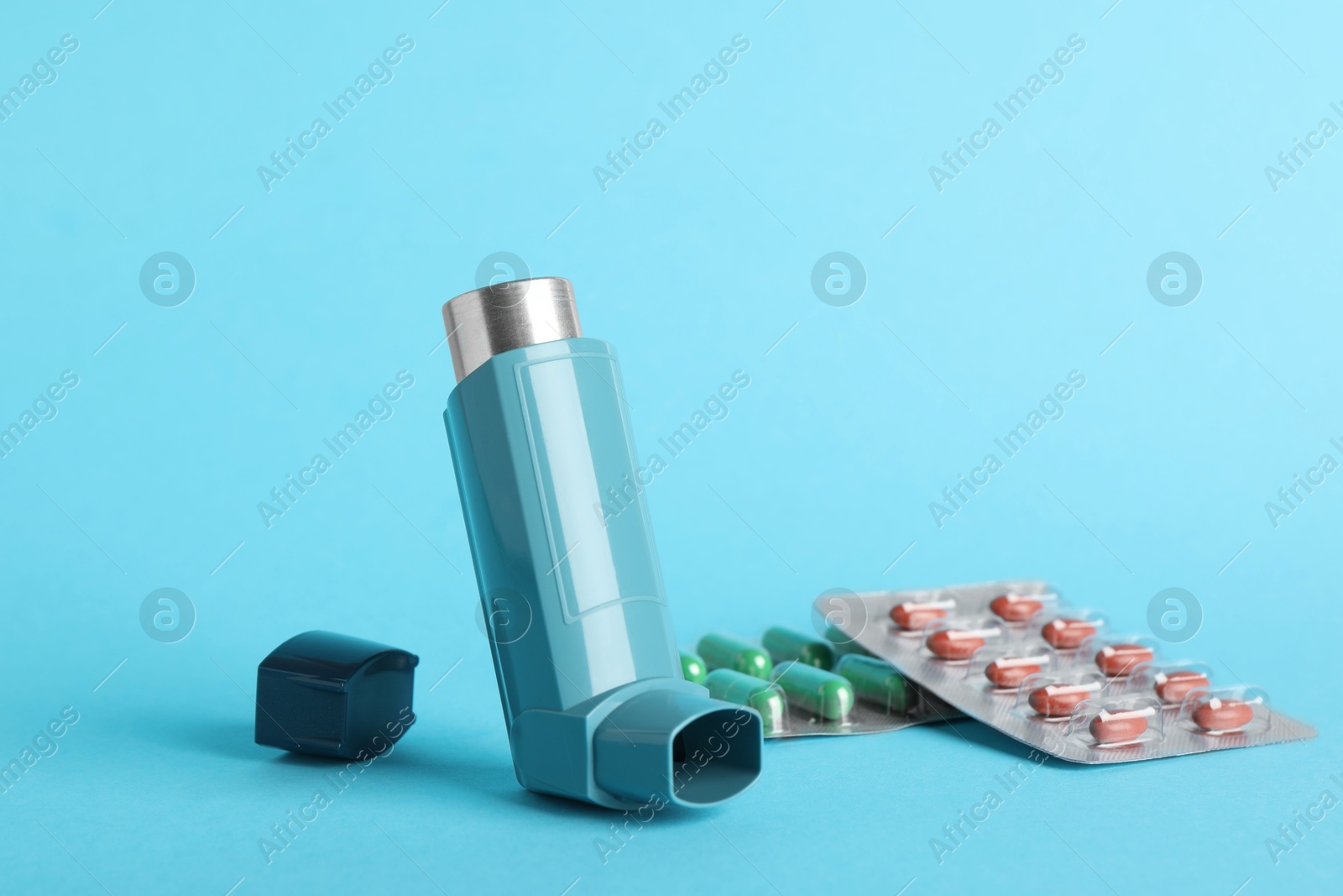 Photo of Inhaler and pills on light blue background, closeup. Asthma treatment