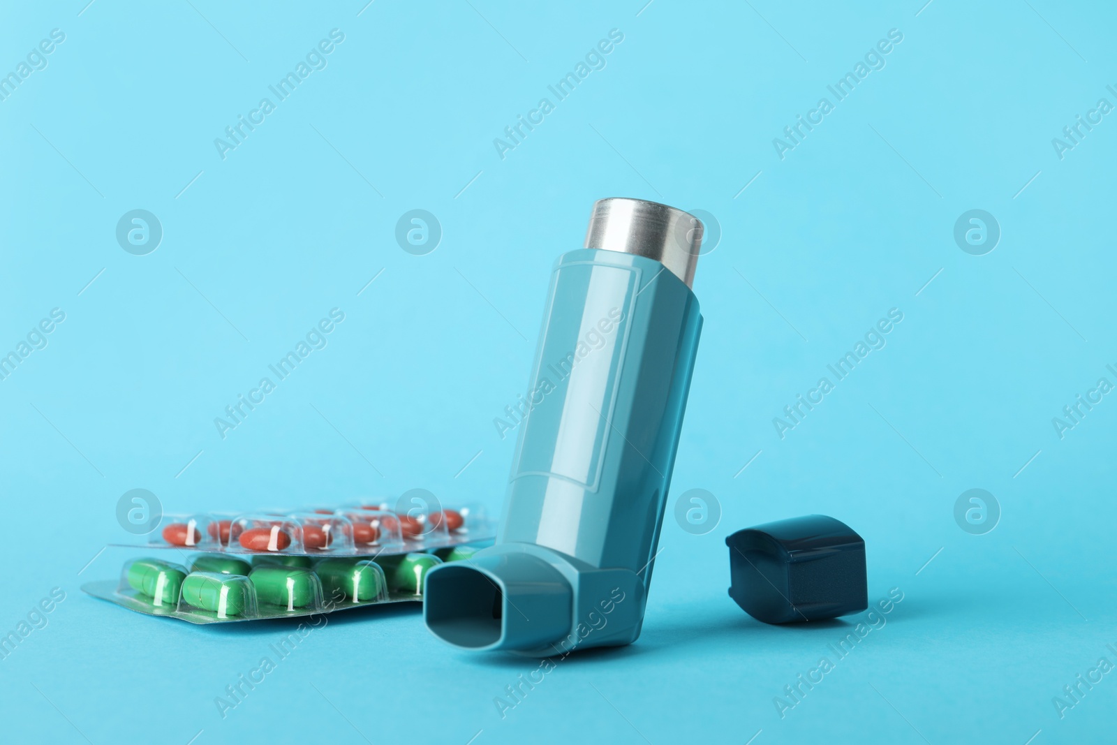 Photo of Inhaler and pills on light blue background, closeup. Asthma treatment