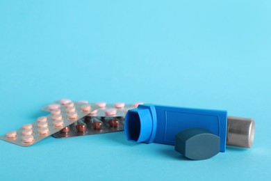 Photo of Inhaler and pills on light blue background, closeup. Asthma treatment