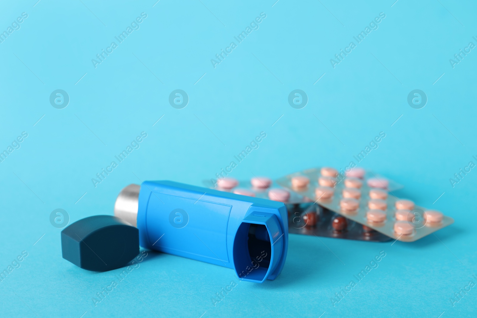 Photo of Inhaler and pills on light blue background, closeup. Asthma treatment