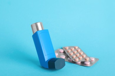 Photo of Inhaler and pills on light blue background, closeup. Asthma treatment