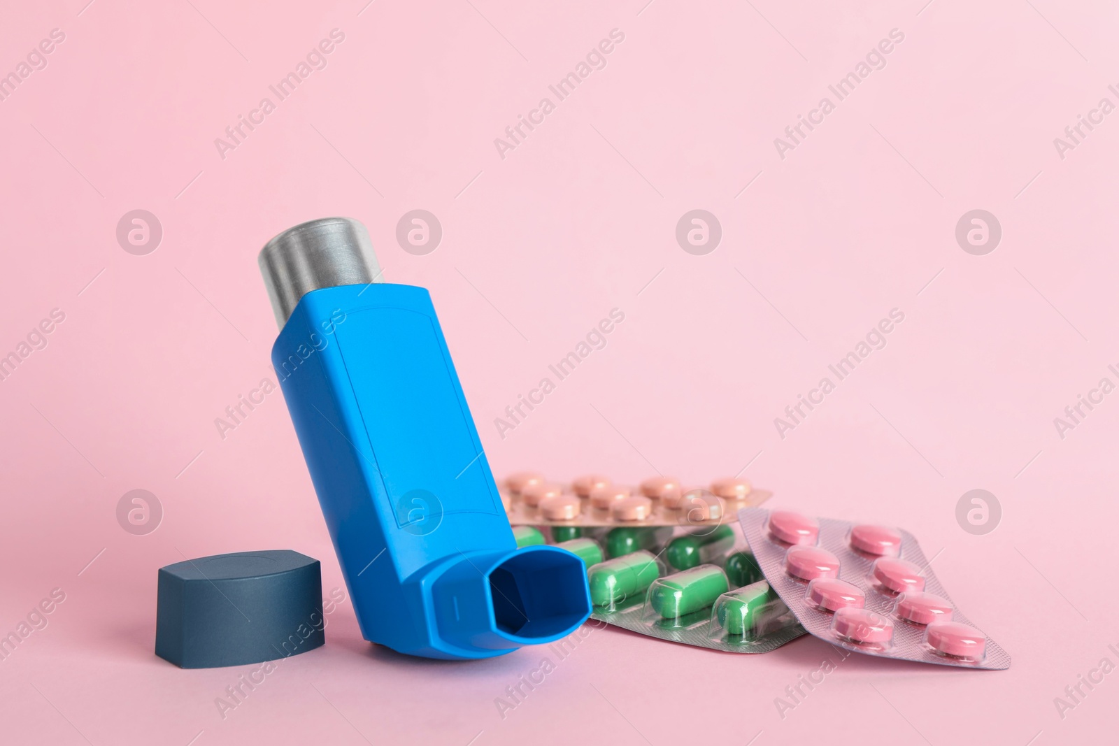 Photo of Inhaler and pills on pink background, closeup with space for text. Asthma treatment