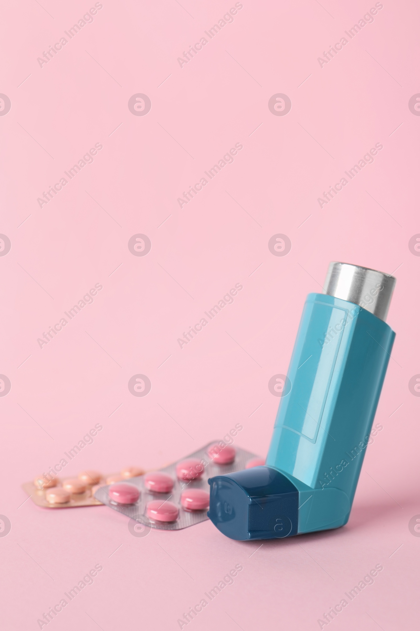 Photo of Inhaler and pills on pink background, closeup. Asthma treatment