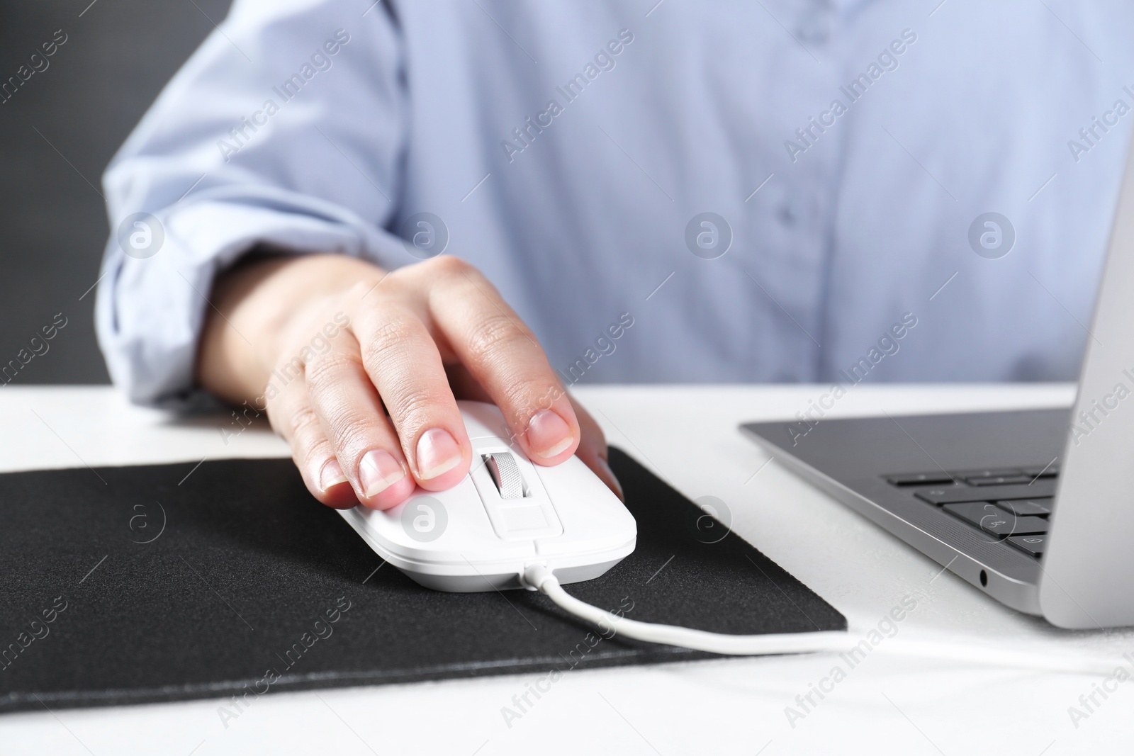 Photo of Woman using computer mouse while working with laptop at white table, closeup