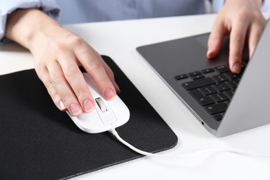 Photo of Woman using computer mouse while working with laptop at white table, closeup