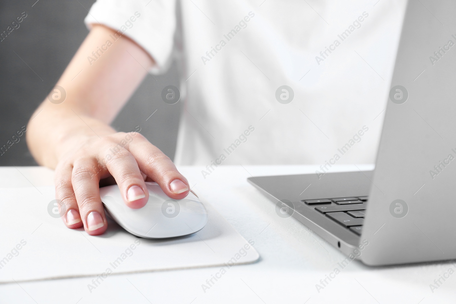 Photo of Woman using computer mouse while working with laptop at white table, closeup