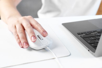 Photo of Woman using computer mouse while working with laptop at white table, closeup