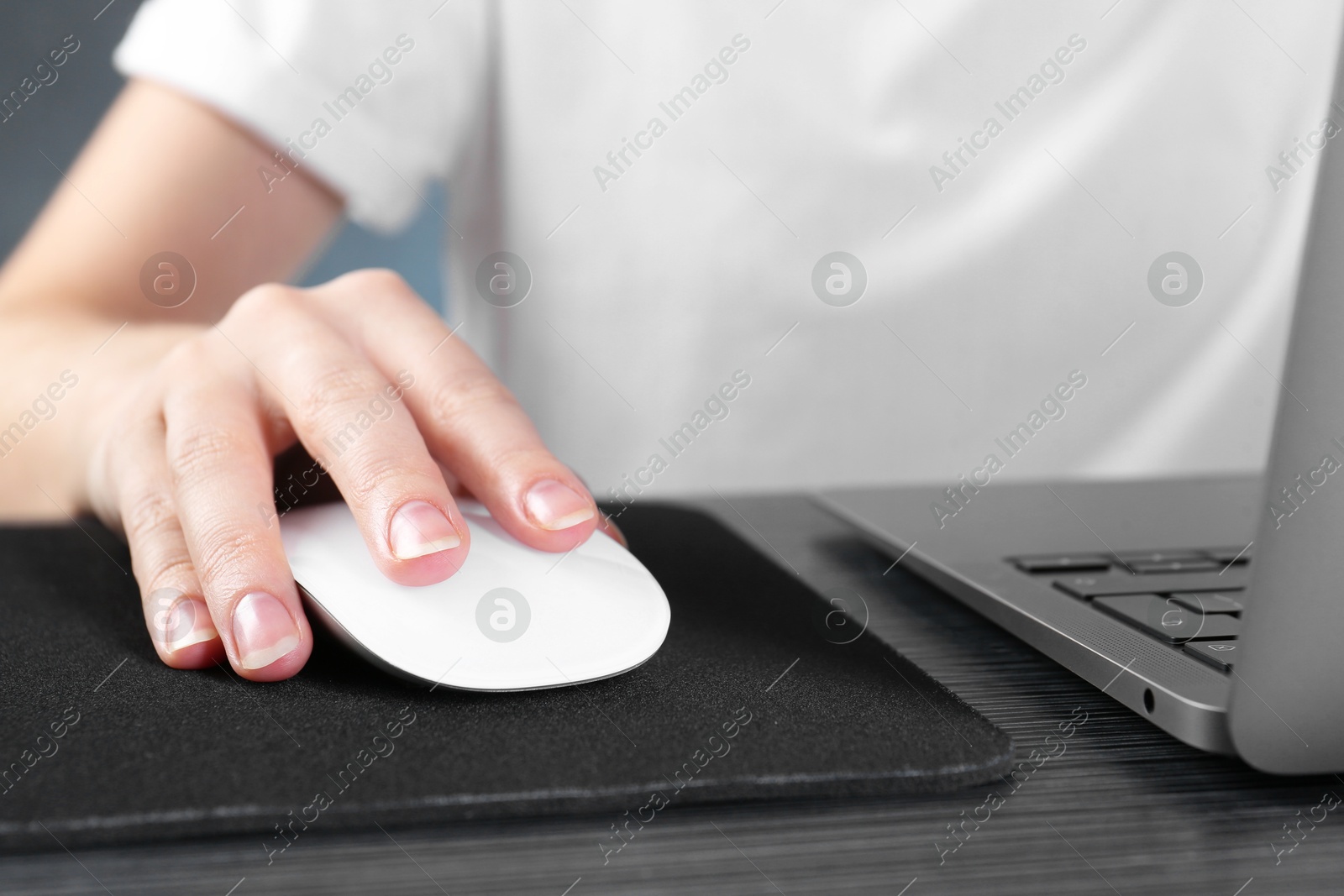 Photo of Woman using computer mouse while working with laptop at black wooden table, closeup