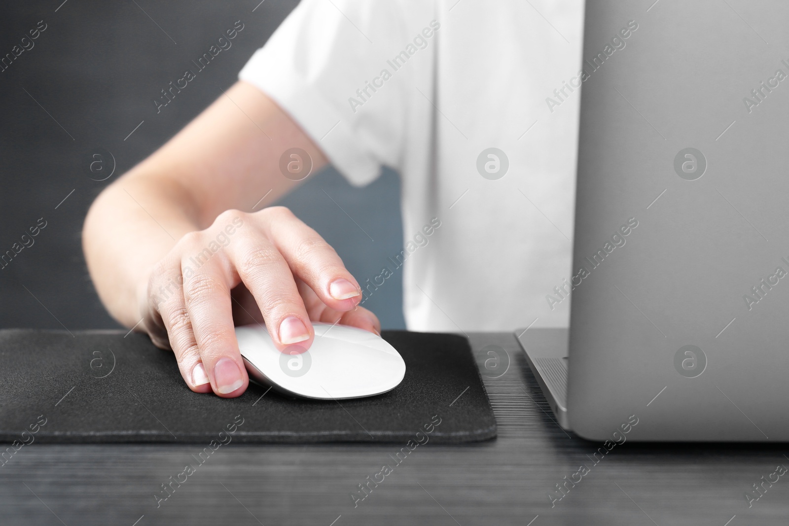 Photo of Woman using computer mouse while working with laptop at black wooden table, closeup