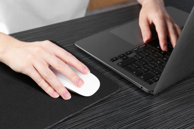 Photo of Woman using computer mouse while working with laptop at black wooden table, closeup