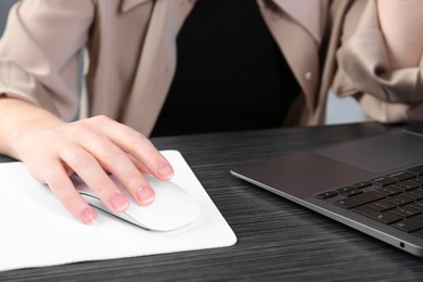 Photo of Woman using computer mouse while working with laptop at black wooden table, closeup