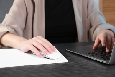 Photo of Woman using computer mouse while working with laptop at black wooden table, closeup