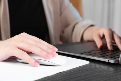 Photo of Woman using computer mouse while working with laptop at black wooden table, closeup