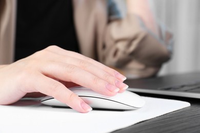 Photo of Woman using computer mouse while working with laptop at black wooden table, closeup