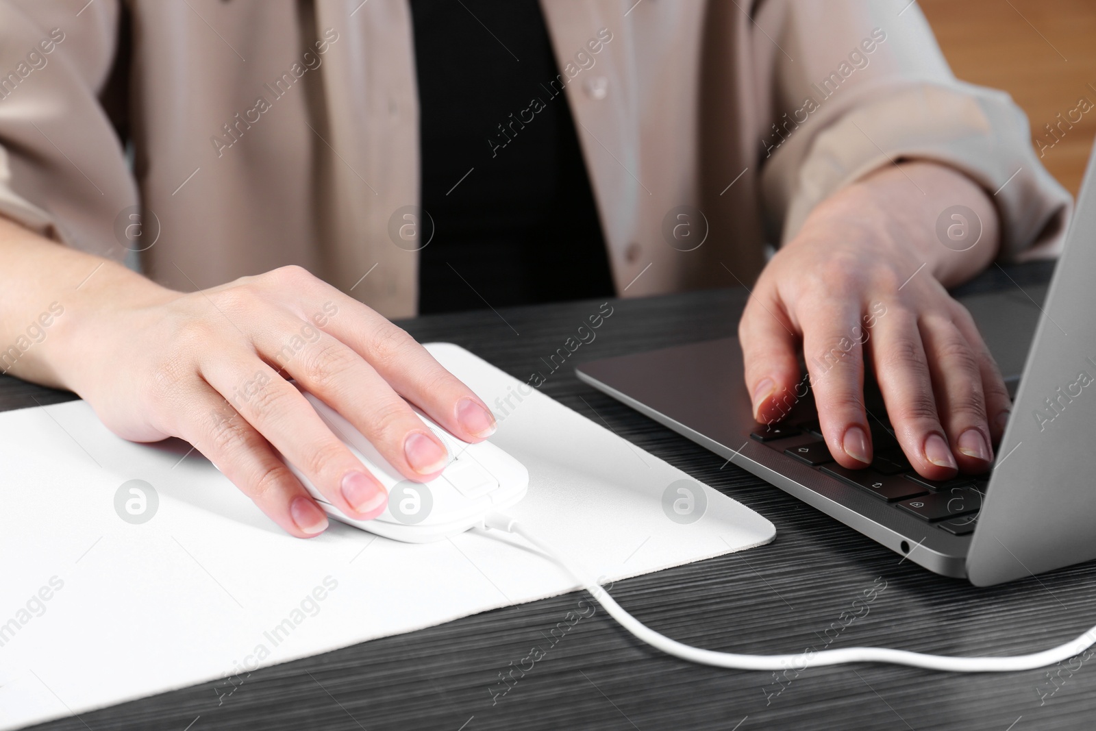 Photo of Woman using computer mouse while working with laptop at black wooden table, closeup