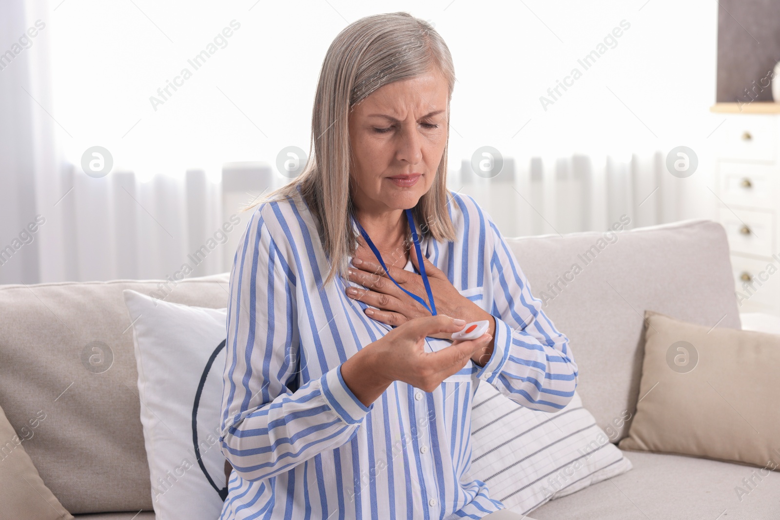 Photo of Senior woman suffering from heart pain pressing emergency call button at home