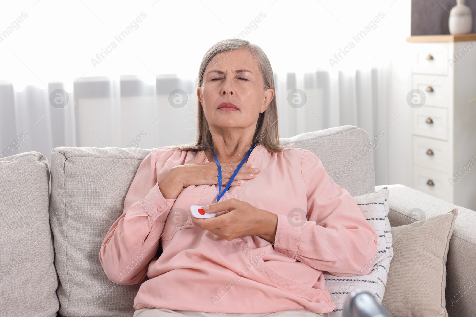 Photo of Senior woman suffering from heart pain pressing emergency call button at home