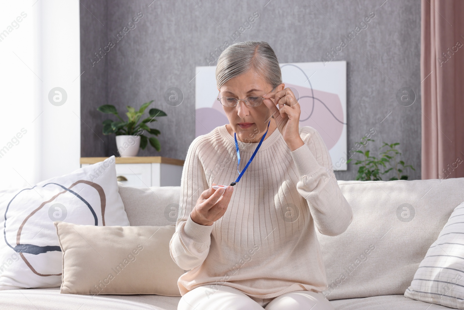 Photo of Senior woman in glasses with emergency call button at home