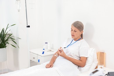 Senior woman with emergency call button on bed in hospital