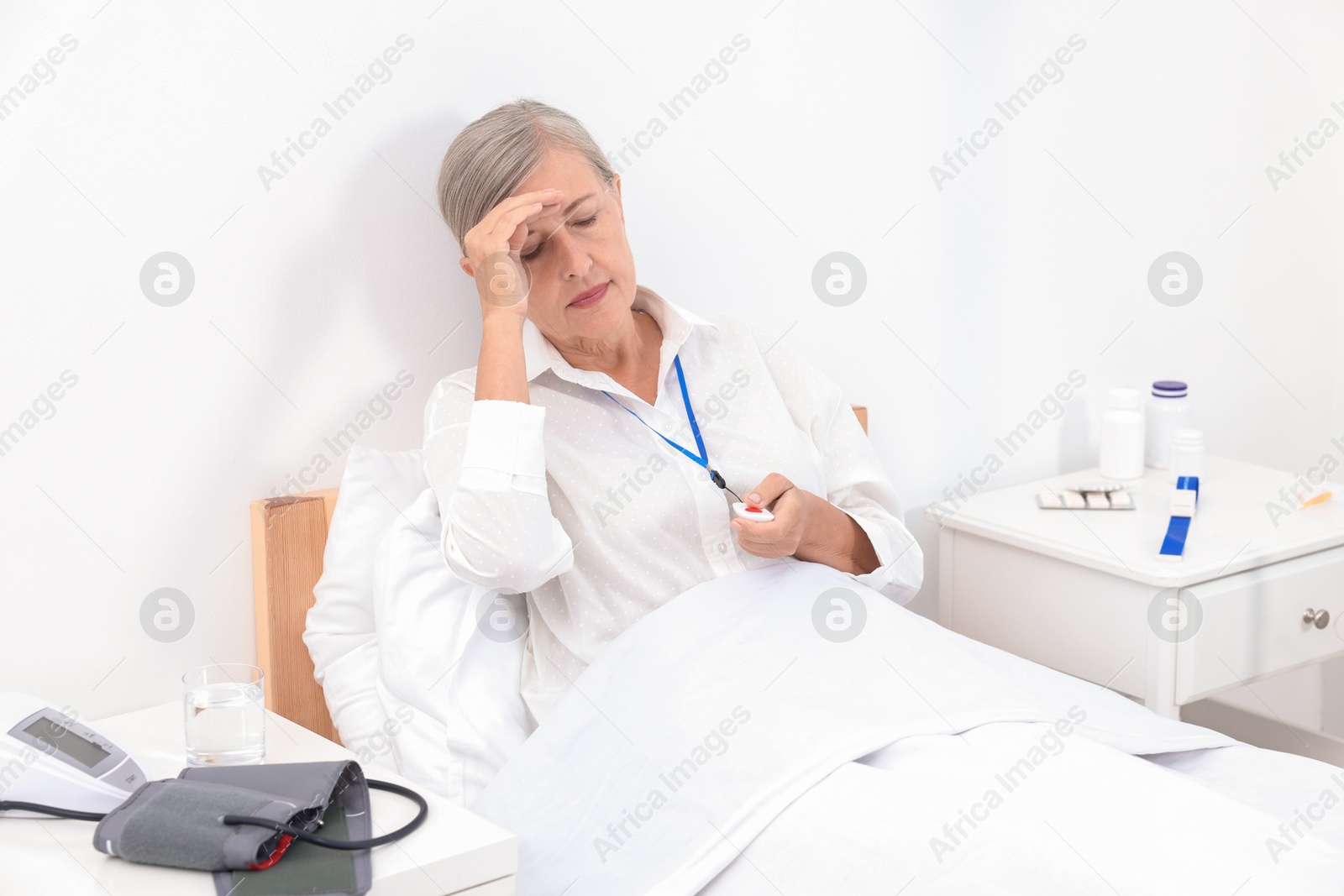 Photo of Senior woman suffering from headache pressing emergency call button on bed in hospital