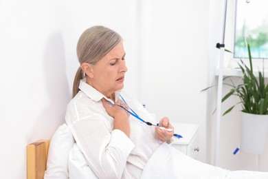 Photo of Senior woman suffering from heart pain pressing emergency call button on bed in hospital