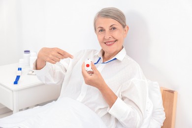 Happy senior woman pointing at emergency call button in hospital