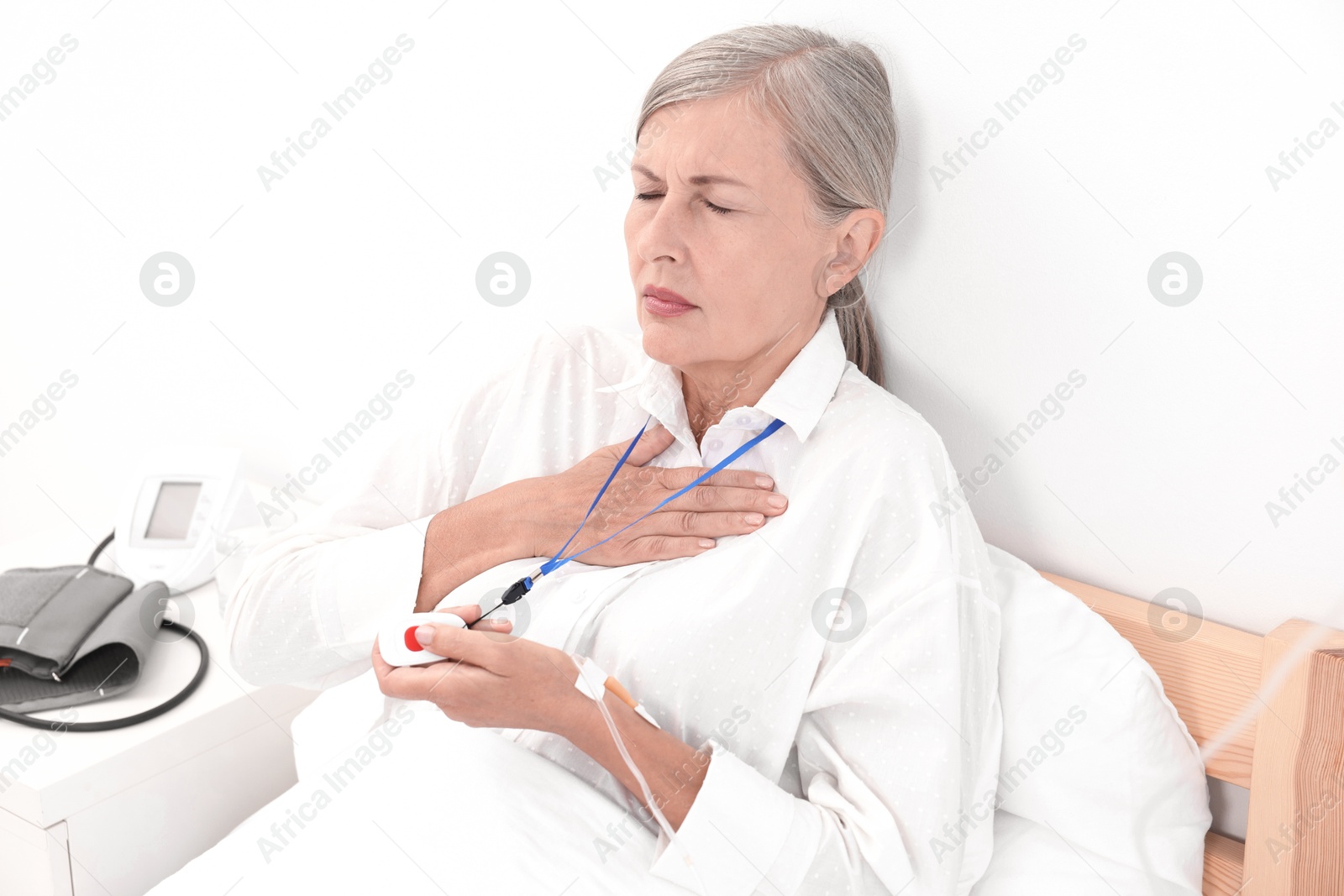 Photo of Senior woman suffering from heart pain pressing emergency call button on bed in hospital