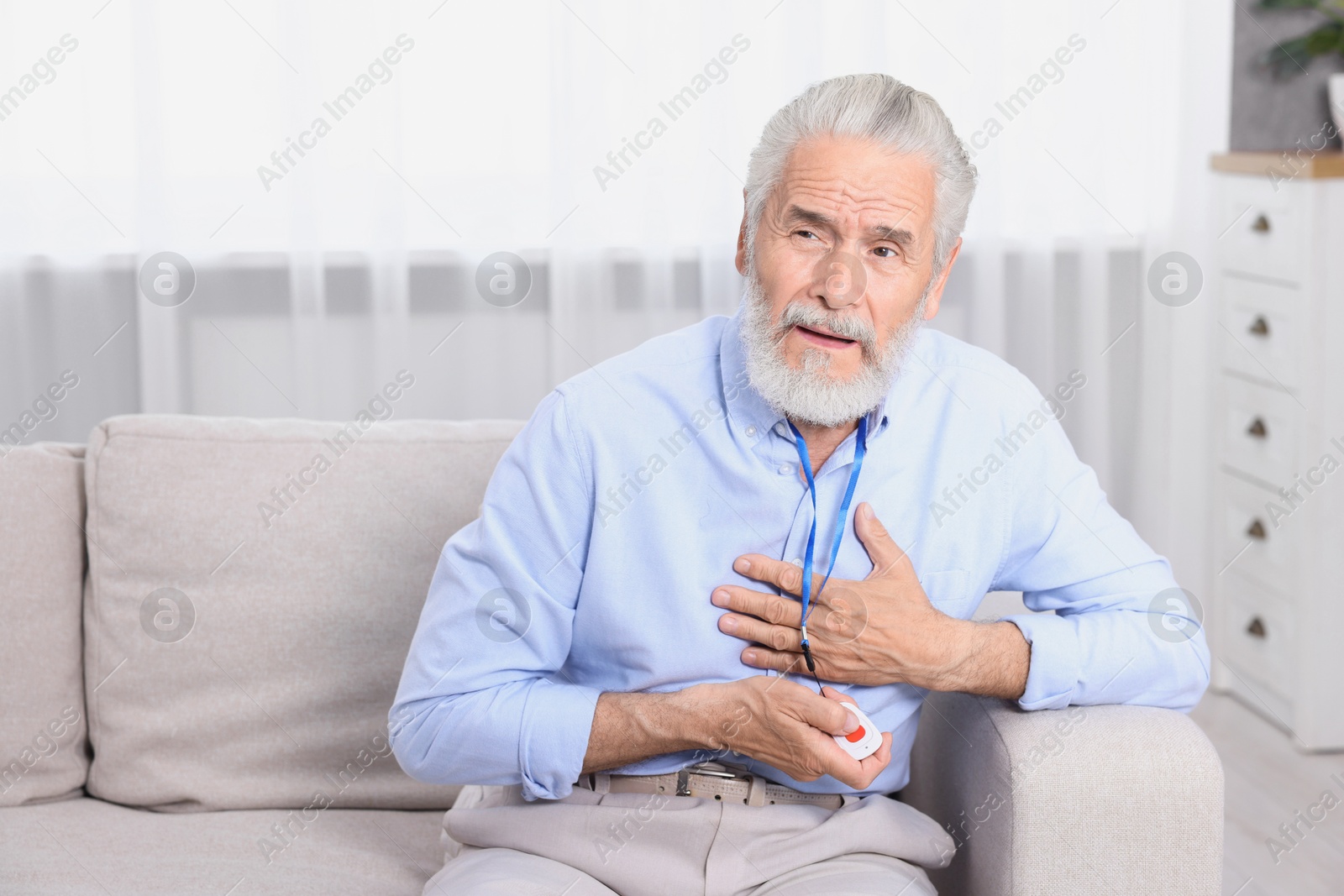 Photo of Senior man suffering from heart pain pressing emergency call button at home