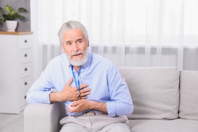 Photo of Senior man suffering from heart pain pressing emergency call button at home