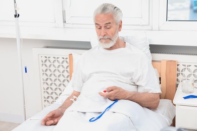 Senior man pressing emergency call button on bed in hospital