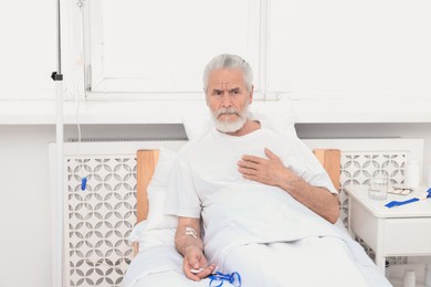 Photo of Senior man suffering from heart pain pressing emergency call button on bed in hospital