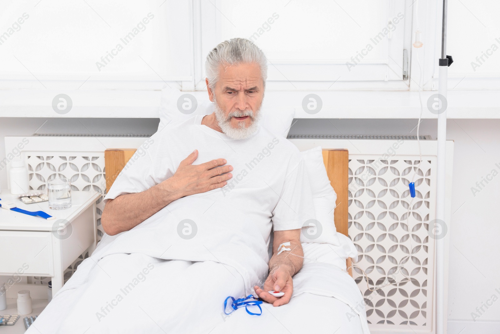 Photo of Senior man suffering from heart pain pressing emergency call button on bed in hospital