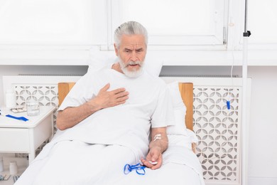 Senior man suffering from heart pain pressing emergency call button on bed in hospital