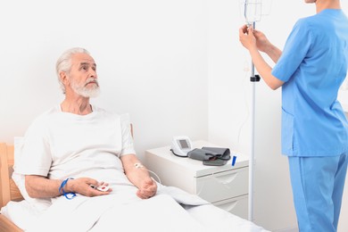 Senior man with emergency call button and nurse setting IV drip in hospital, closeup