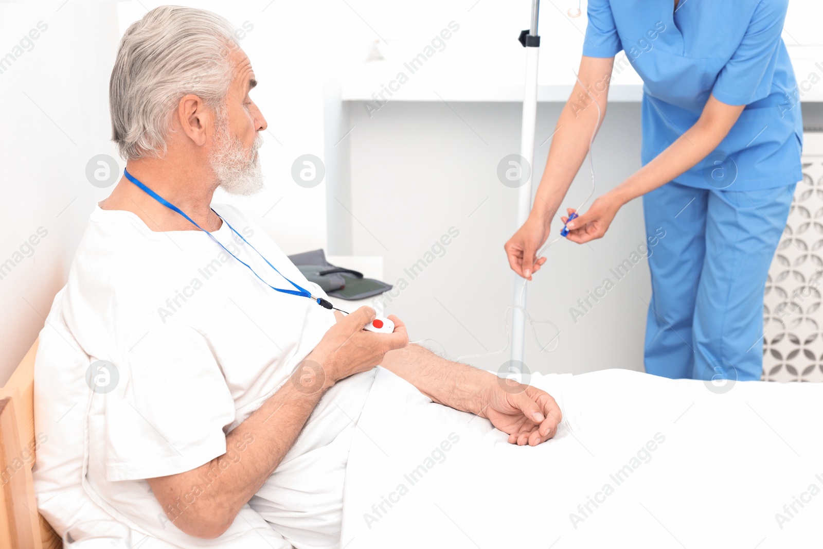 Photo of Senior man with emergency call button and nurse setting IV drip in hospital, closeup