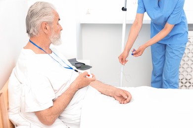 Photo of Senior man with emergency call button and nurse setting IV drip in hospital, closeup