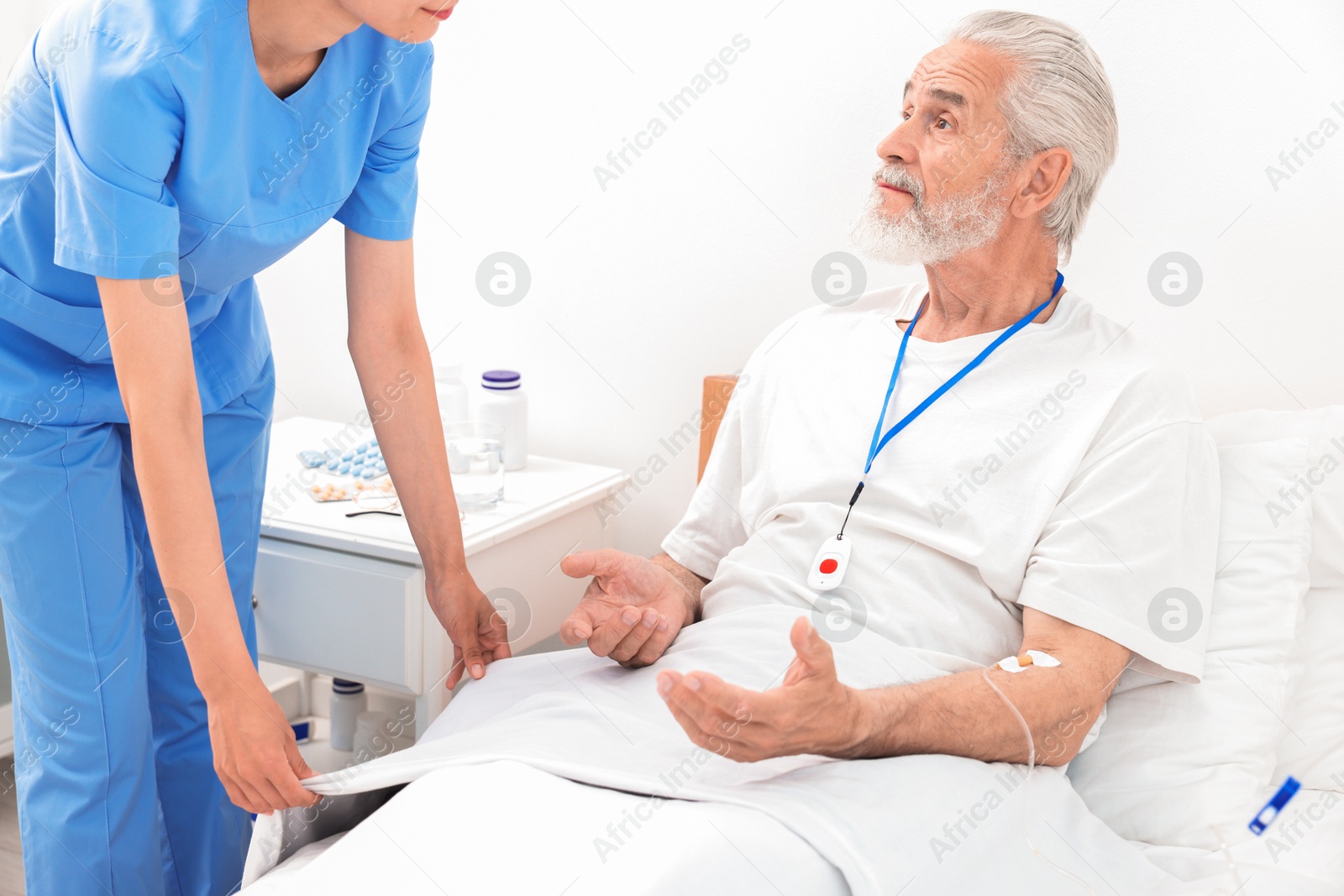 Photo of Senior man with emergency call button talking to nurse in hospital