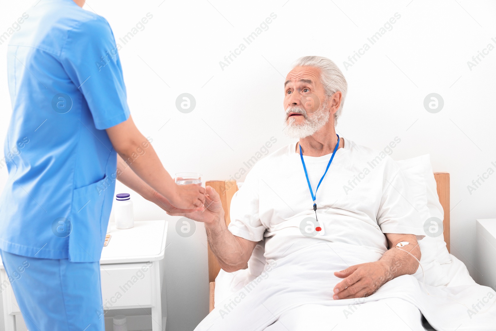 Photo of Senior man with emergency call button taking glass of water nurse giving him in hospital, closeup