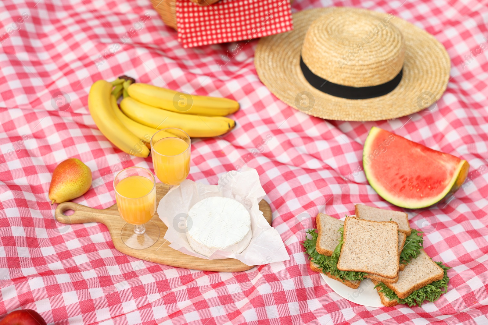 Photo of Different food, juice and hat on picnic blanket, closeup